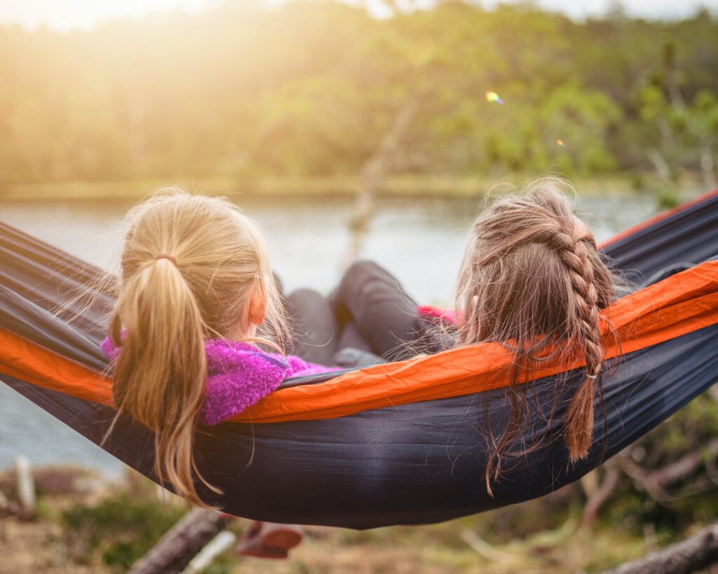 duas meninas estão deitadas em uma rede vendo o pôr do sol